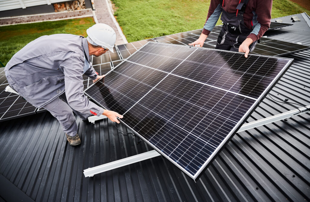 Technicians Carrying Photovoltaic Solar Module While Installing Solar Panel System On Roof Of House